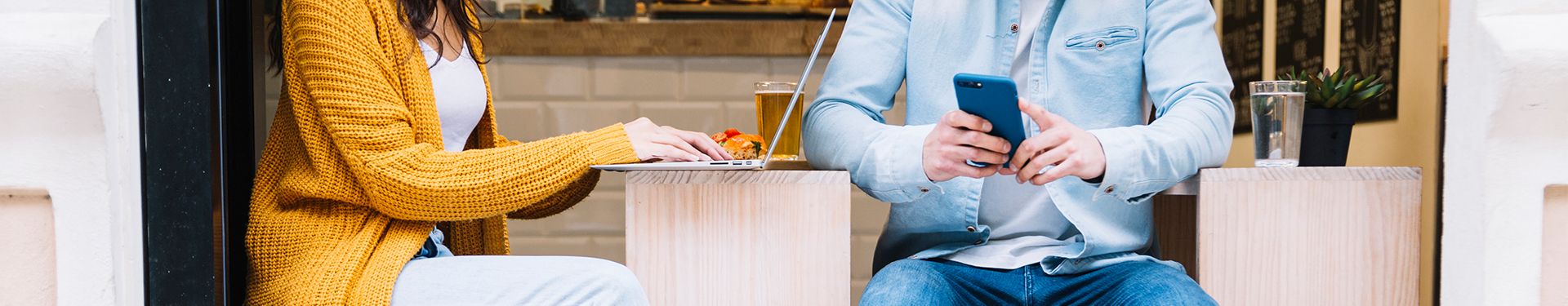 Mann und Frau sitzen mit Handy und Laptop in einem Café 