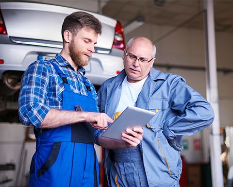 Zwei Mitarbeiter in einer Auto-Werkstatt rufen auf einem Tablet eine Website auf.